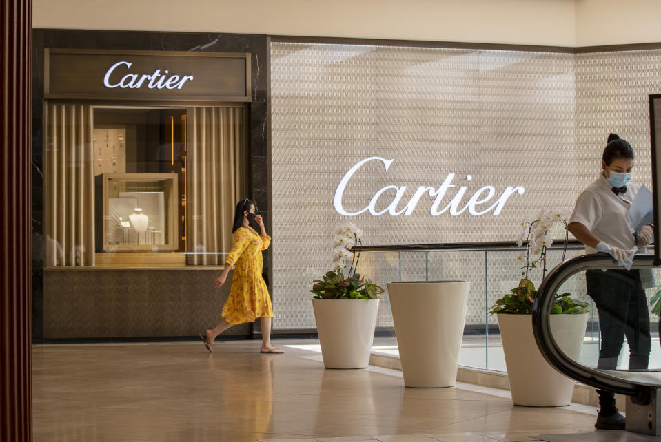 COSTA MESA, CA - JUNE 11: Mall employee Glenby Ramirez, right, wipes down the escalator handrail while a shopper passes by Cartier as South Coast Plaza reopens, requiring customers maintain a social distance and wear face masks at South Coast Plaza Thursday, June 11, 2020 in Costa Mesa, CA. Although not all stores in the upscale shopping center will resume operations, more than 110 merchants - including Apple, Macy's and Nordstrom - are opening their doors after being closed for three months amid the coronavirus pandemic. (Allen J. Schaben / Los Angeles Times via Getty Images)