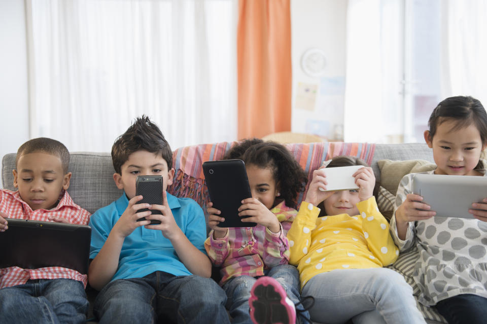 Kids on a couch all playing on smartphones or iPads