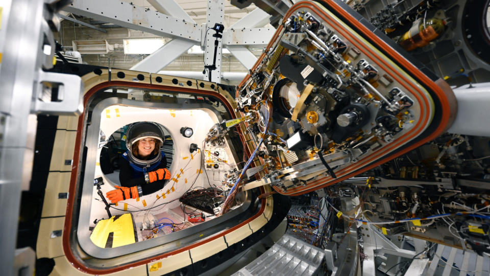 an open spacecraft hatch with christina koch far in the background