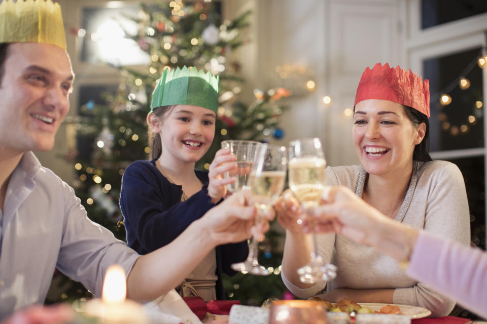 Happy family in paper crows toasting water and champagne glasses at Christmas dinner