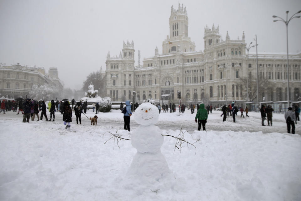 People walk past the Cibeles monument, left, in front of the City Hall during a heavy snowfall in downtown Madrid, Spain, Saturday, Jan. 9, 2021. A persistent blizzard has blanketed large parts of Spain with 50-year record levels of snow, halting traffic and leaving thousands trapped in cars or in train stations and airports that suspended all services as the snow kept falling on Saturday. (AP Photo/Andrea Comas)