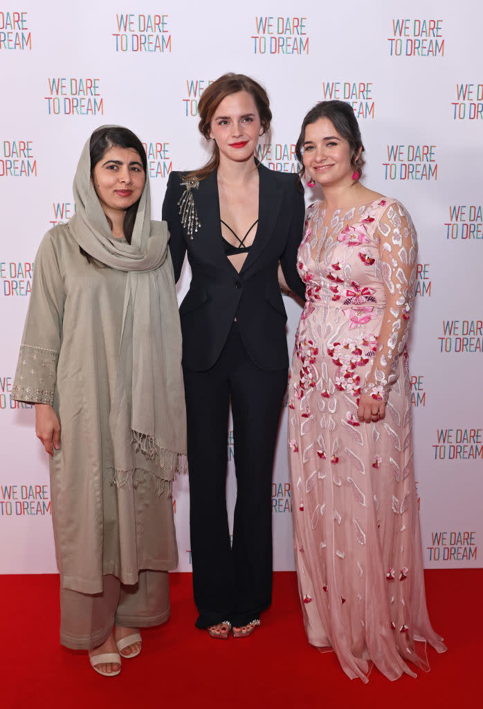 Three women standing together; two in formal dresses and one in a suit, posing at an event