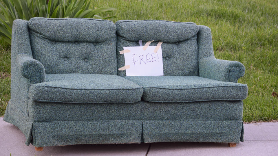 A sofa placed on the sidewalk with a sign marking it free for pick up.