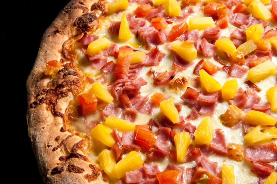 Hawaiian pizza with pineapple and ham is seen close up on a black background.