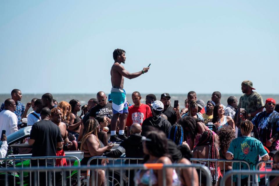 Spring breakers take photos of cars parked along Highway 90 during Black Spring Break in Biloxi on Saturday, April 9, 2022.