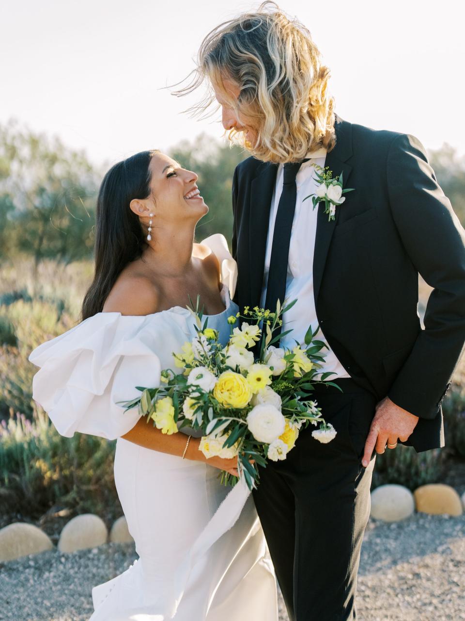 A bride and groom grin at each other on their wedding day.