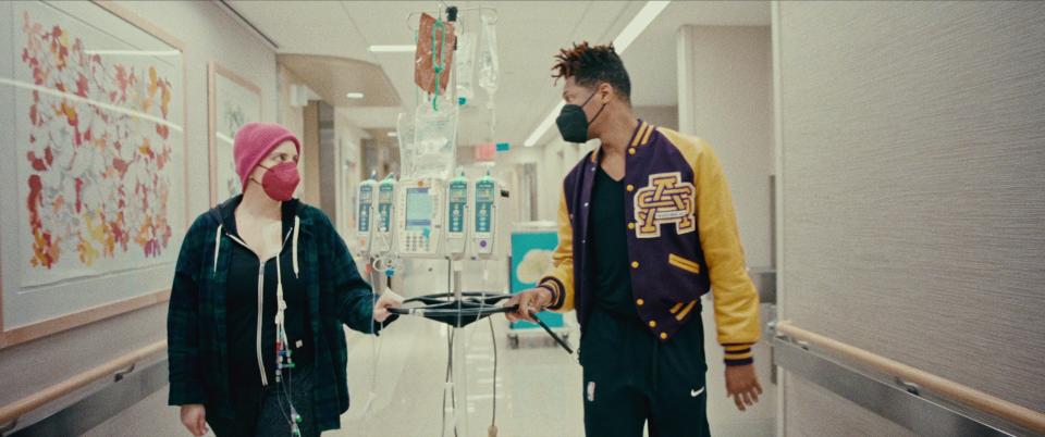 Suleika Jaouad and Jon Batiste walk down a hospital corridor during her leukemia treatment in the Netflix documentary "American Symphony."