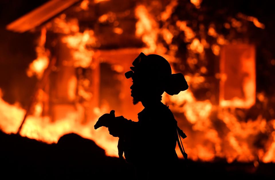 A firefighter is silhouetted as a house burns in the background.