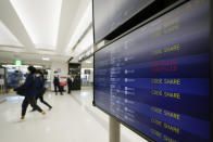 Passengers walk by arrival information screens for international flights at the Narita International Airport in Narita, east of Tokyo, Thursday, Dec. 2, 2021. Going further than many other countries in trying to contain the virus, Japan has banned foreign visitors and asked international airlines to stop taking new reservations for all flights arriving in the country until the end of December. (AP Photo/Hiro Komae)