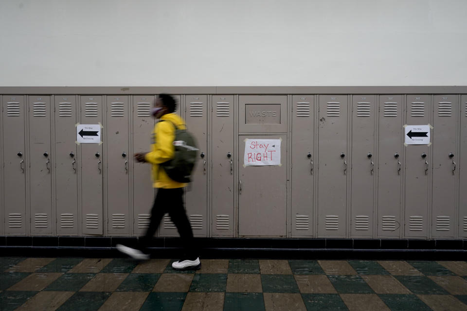 FILE - In this March 31, 2021, file photo, a student walks on the right side of a hallway to avoid contact with other students at Wyandotte County High School on the first day of in-person learning at the school in Kansas City, Kan. With a massive infusion of federal aid coming their way, schools across the U.S. are weighing how to use the windfall to ease the harm of the pandemic — and to tackle problems that existed long before the coronavirus. (AP Photo/Charlie Riedel, File)