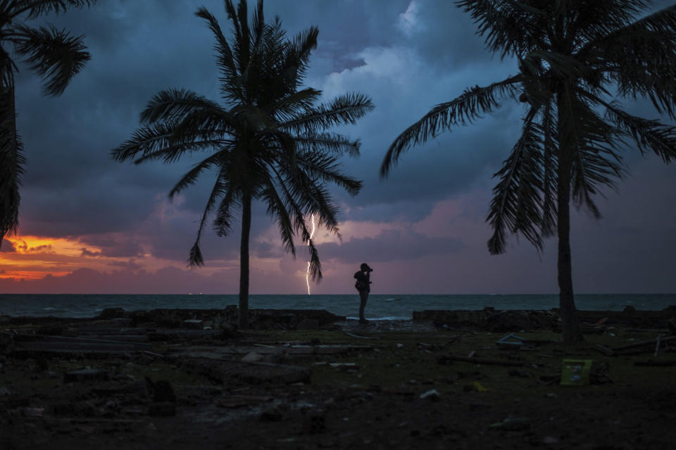 In this Tuesday, Dec. 25, 2018, file photo, a photojournalist is silhouetted by the sunset as a lightning strike at a resort affected by Saturday's tsunami in Carita, Indonesia. Christmas celebrations traditionally filled with laughter and uplifting music were replaced by somber prayers for tsunami victims in an area hit without warning following a volcanic eruption, leaving hundreds of people dead and thousands homeless in disaster-prone Indonesia. (AP Photo/Fauzy Chaniago, File)
