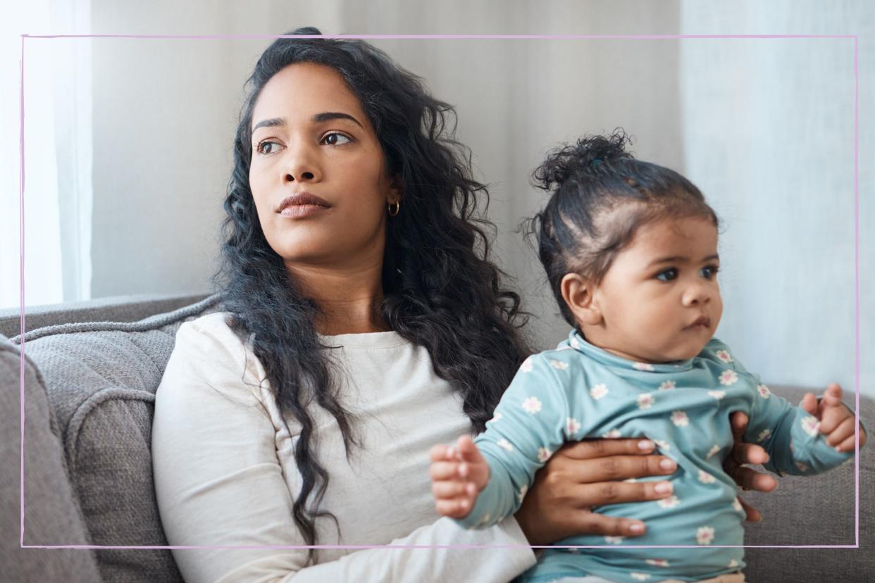  Concerned-looking mother holding baby daughter on the sofa. 