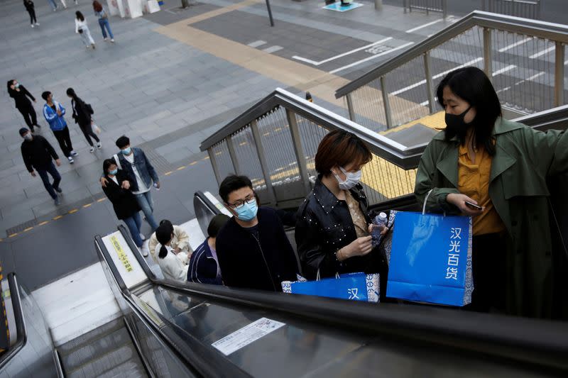 People wearing face masks carry shopping bags as they ride an escalator at a shopping area during Chinese Qingming festival holiday in Beijing