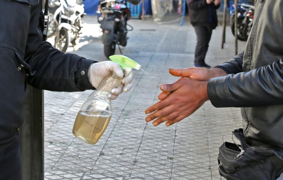 An Iranian man sprays alcohol on the hands of people outside an office building in Tehran on March 4. Source: Getty Images 