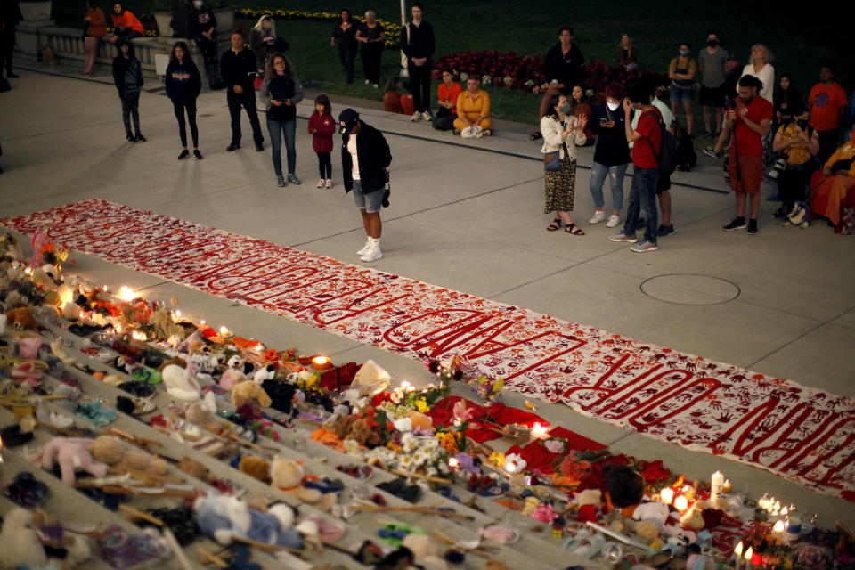 People pay respects to the victims of Canada's residential school system amid shoes, teddy bears, orange shirts and other tributes placed on the steps outside the legislature, in Victoria, Thursday, July 1, 2021. (Chad Hipolito/The Canadian Press via AP)