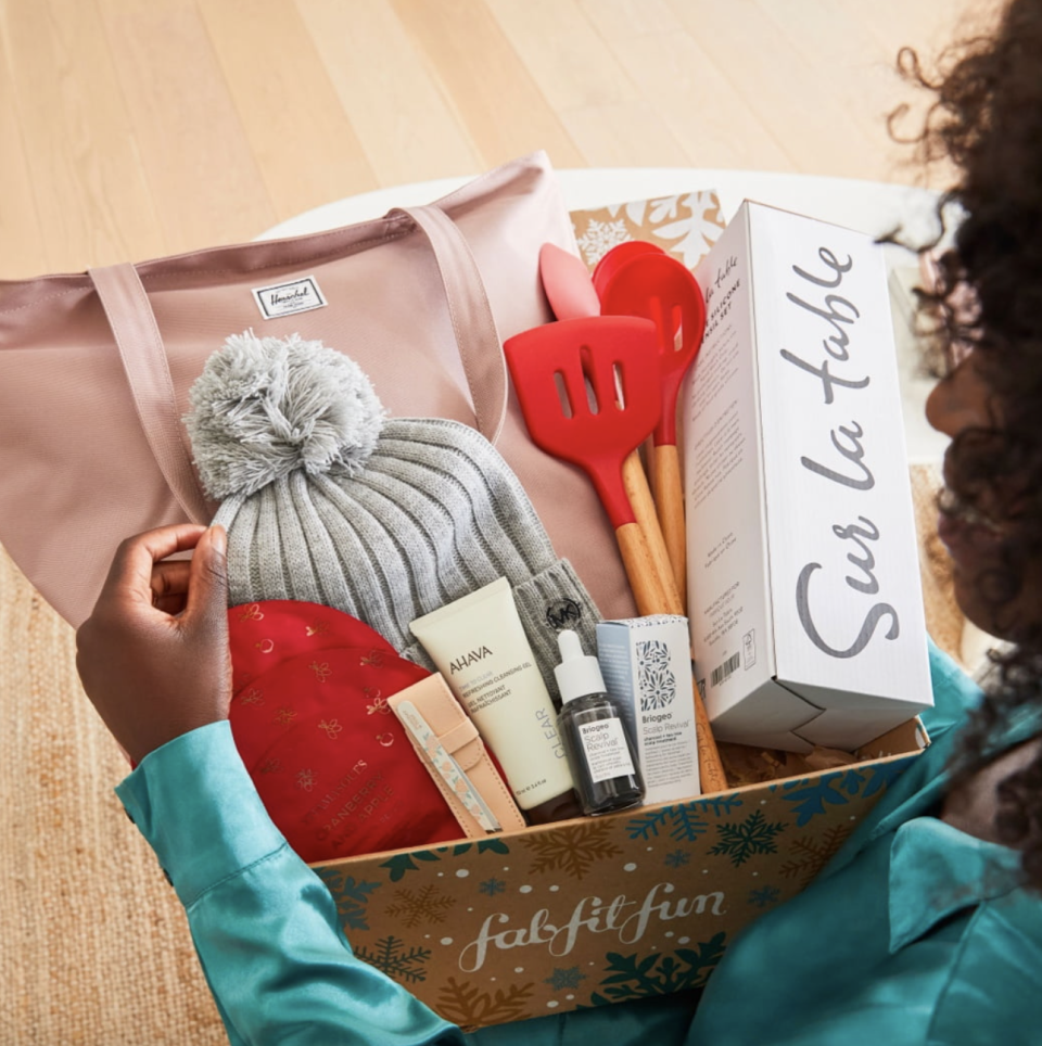 woman holding FabFitFun box with bag, toque, kitchen utensils, beauty supplies