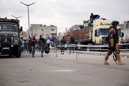 People carry their belongings as they walk near a Russian soldier (R), as rebel fighters and their families evacuate the besieged Waer district, after an agreement reached between rebels and Syria's army, in Homs, Syria May 20, 2017. REUTERS/Omar Sanadiki