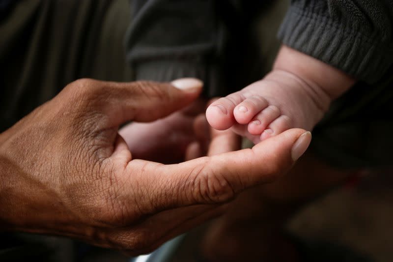 A Central American migrant touches his son's foot at an encampment of more than 2,000 migrants, as local authorities prepare to respond to the coronavirus disease (COVID-19) outbreak, in Matamoros