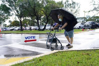 Franklin Castellon, 76, shields himself from the rain as he walks to an early voting site, Monday, Oct.19, 2020, in Miami. Florida begins in-person early voting Monday in much of the state as the Trump campaign tries to cut into an early advantage Democrats have posted in mail-in votes in the key swing state. (AP Photo/Lynne Sladky)