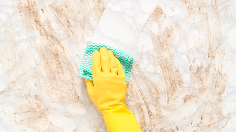 Yellow gloved hand wiping marble countertop clean
