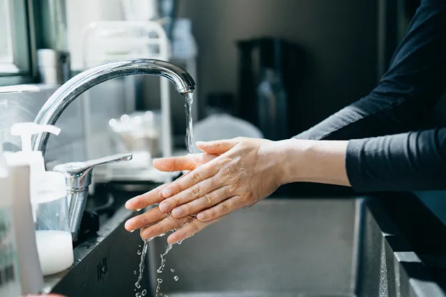 Cropped shot of a woman washing hands with soap in the kitchen sink, illustrating a story on rising water prices.
