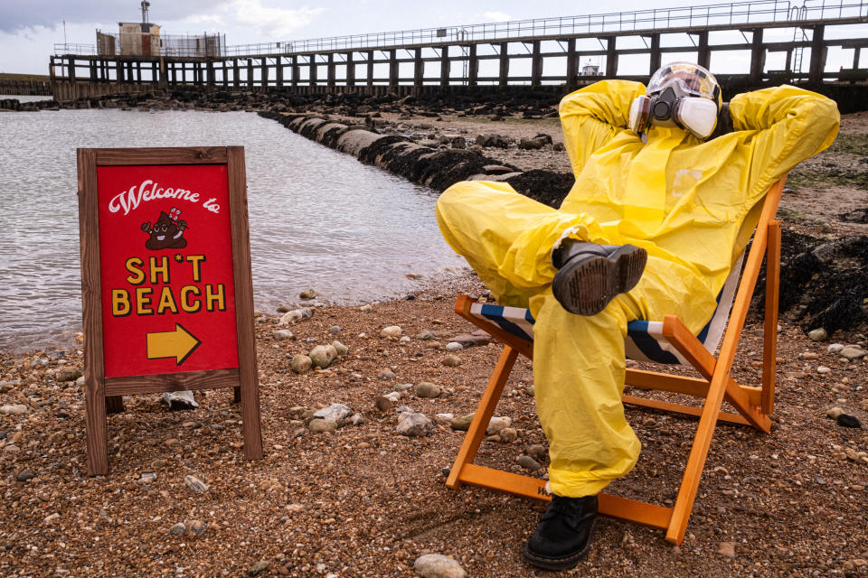 A person in protective yellow clothing sits on a deckchair on a beach