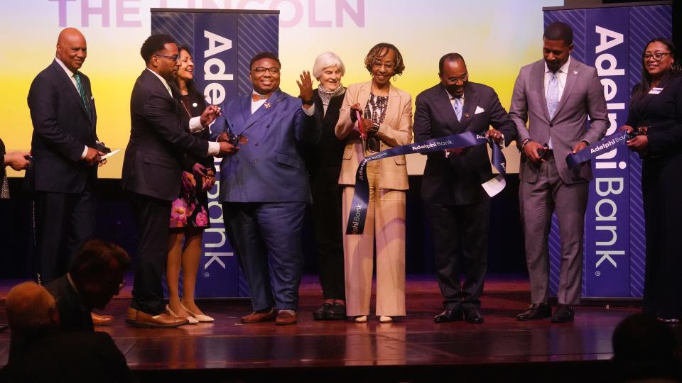 Representative Dontavius L. Jarrells (center, blue shirt) gestures as the ribbon falls on the new Adelphi Bank. Hundreds took part in the Lincoln Theatre ceremony for  Adelphi, which is currently the only Black-owned bank in Ohio.