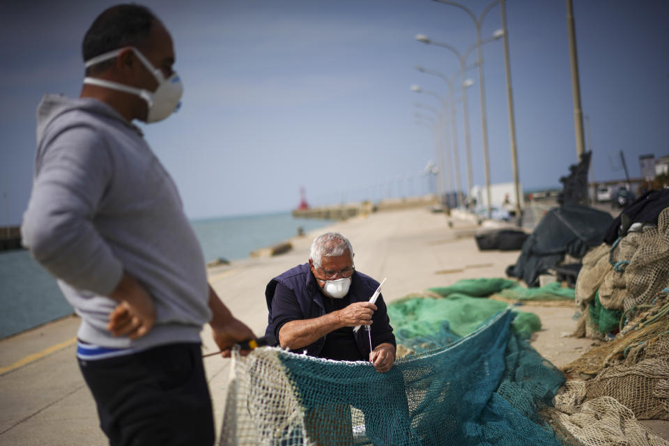 An elderly man repairs a fishing net as an assistant holds up the net, on the empty dock of Fiumicino fishing port, on the outskirts of Rome, Monday, March 30, 2020. On Sundays, or any sunny day throughout the year, you can find several people strolling along, but since the Italian government ordered a nationwide lockdown and shut restaurants and cafés to stop the spread of Covid-19, the area is deserted, and apart from the water rippling against the quay, it is silent. (AP Photo/Andrew Medichini)