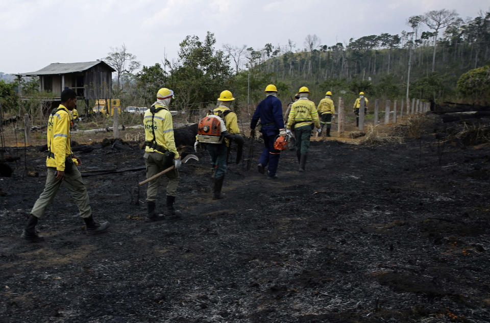 Firefighters walk across charred land to another area as they work to put out fires in the Vila Nova Samuel region, along the road to the National Forest of Jacunda, near the city of Porto Velho, in Rondonia state, part of Brazil's Amazon, Sunday, Aug. 25, 2019. Leaders of the Group of Seven nations said Sunday they were preparing to help Brazil fight the fires burning across the Amazon rainforest and repair the damage even as tens of thousands of soldiers were being deployed to fight the blazes that have caused global alarm. (AP Photo/Eraldo Peres)