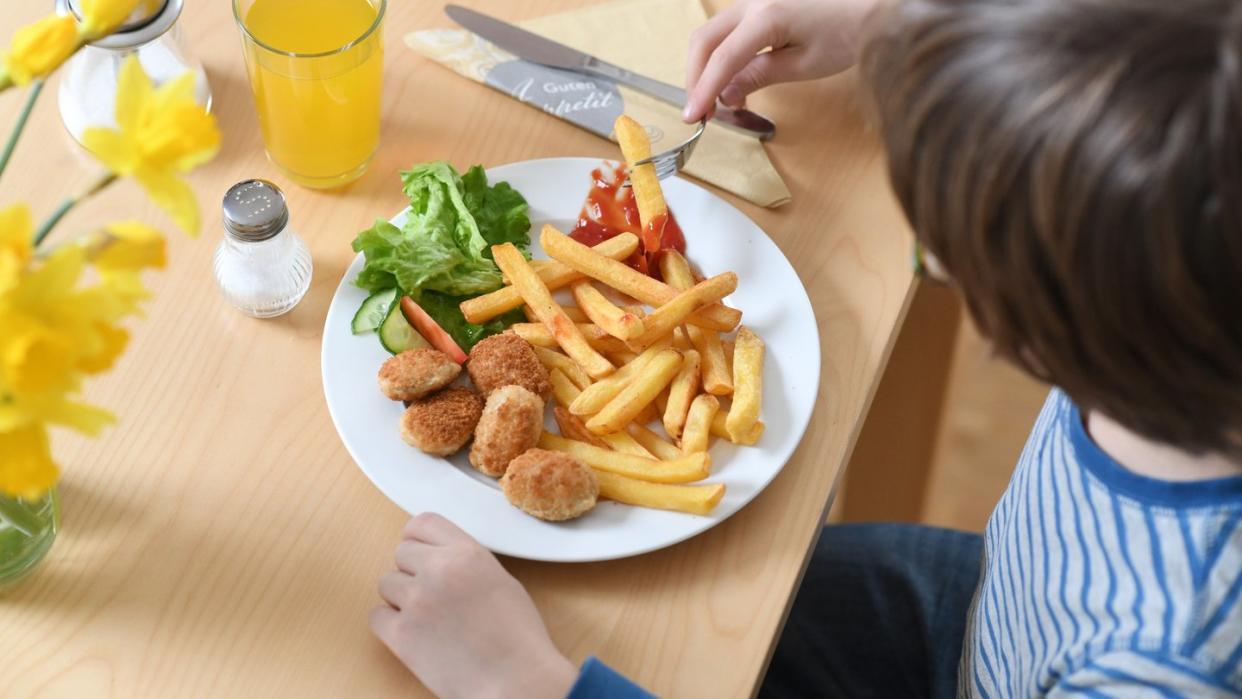 Ein Junge sitzt vor einem Teller mit Chicken Nuggets und Pommes Frites (Archiv). Foto: Tobias Hase