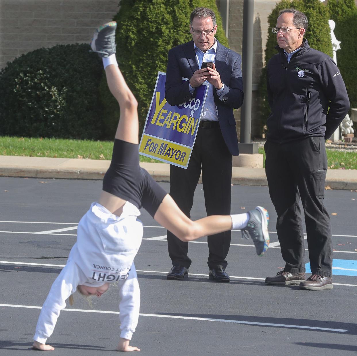 Emma Speight, 9, of Green, does a cartwheel in the parking lot of Queen of Heaven Catholic Church while waiting to talk to voters about her father, City Council candidate Justin Speight, on Tuesday. In the background is mayoral candidate Rocco Yeargin and current Green Mayor Gerard Neugebauer, who is a City Council candidate.