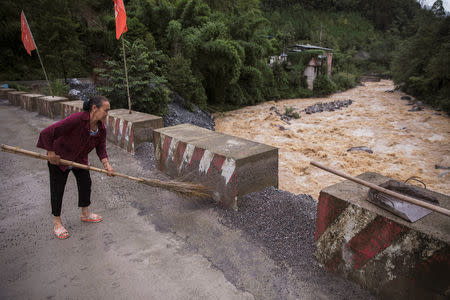A woman sweeps the road in a village that houses a privately-owned small power station on an unnamed tributary of the fierce and flood-prone Dadu river near Leshan in Sichuan province, China, August 3, 2018. REUTERS/Damir Sagolj