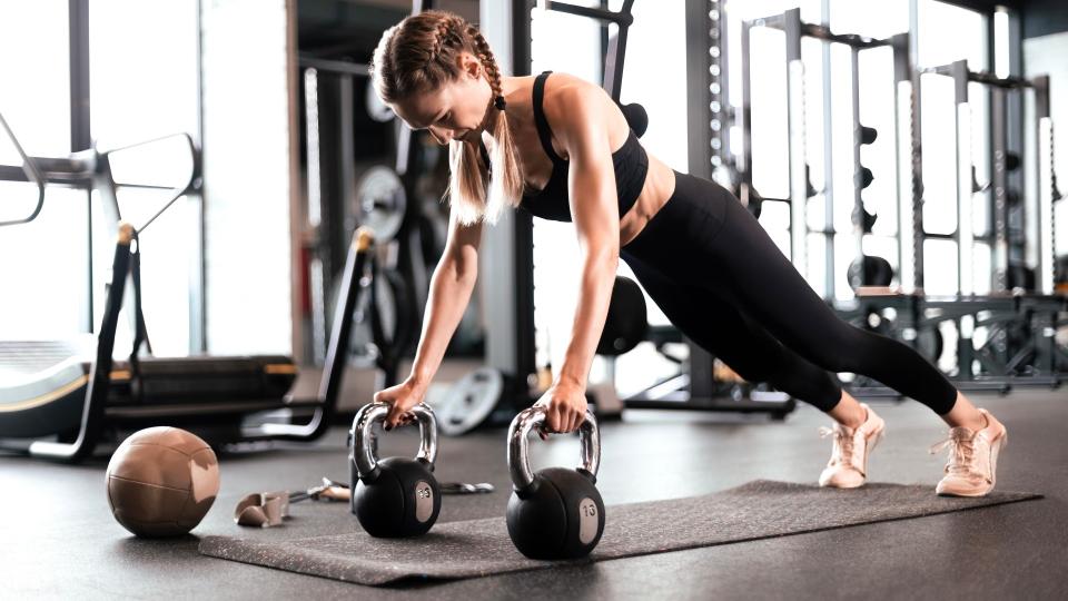 Woman performing a renegade row using two kettlebells