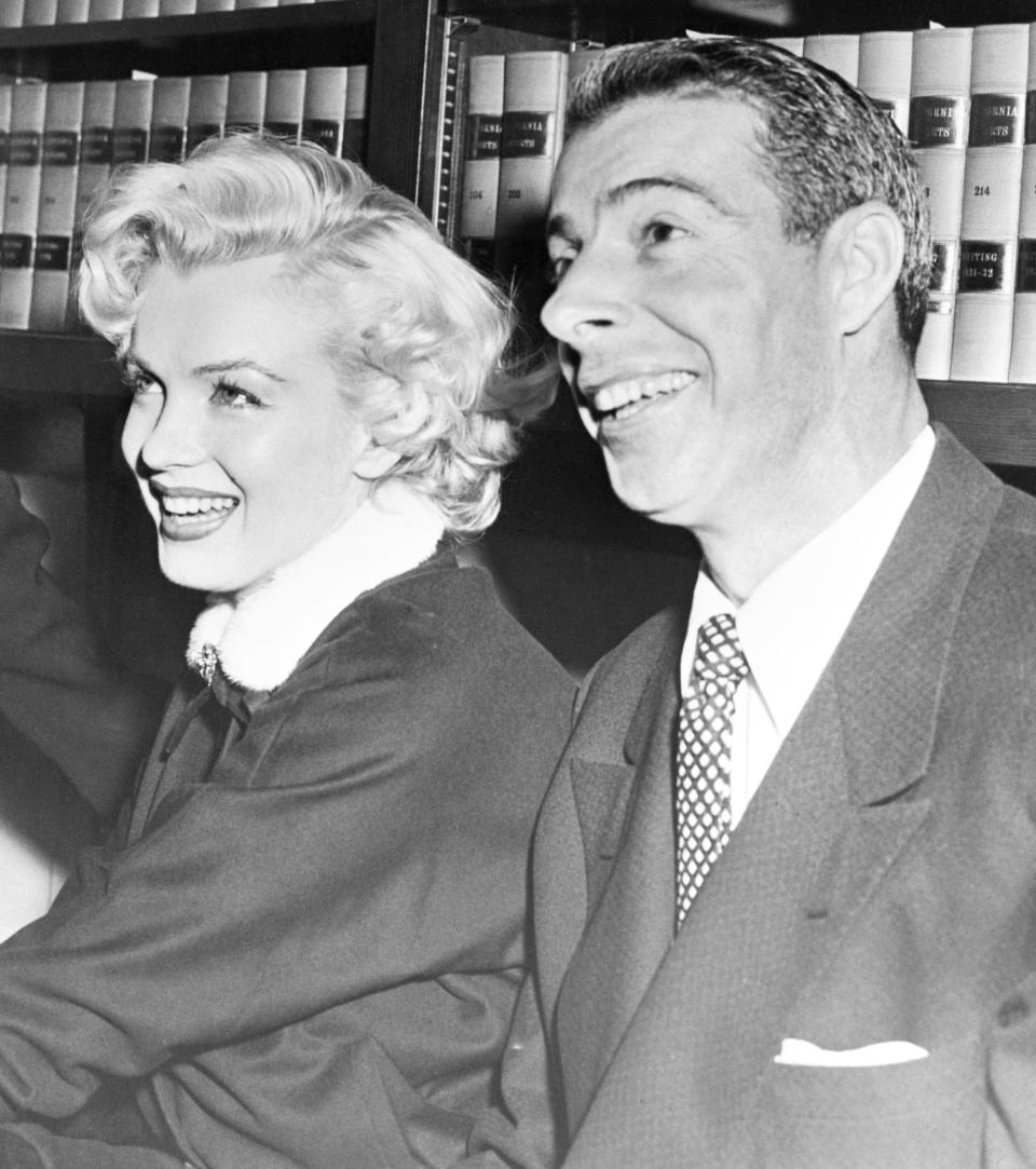 Marilyn Monroe and Joe DiMaggio smile as they look off-camera.