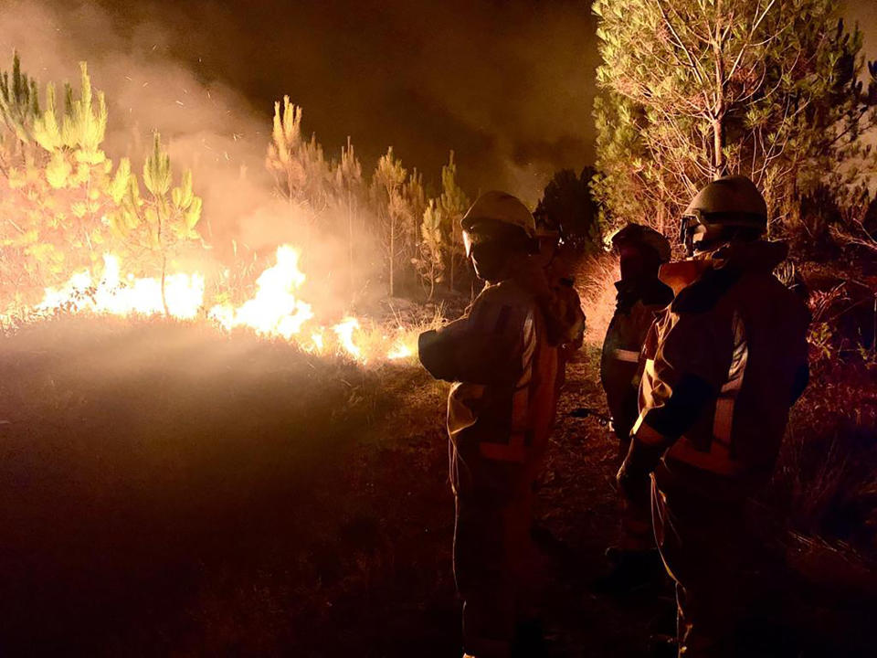 This photo provided by the fire brigade of the Gironde region SDIS 33, (Departmental fire and rescue service 33) shows firefighters observing a blaze near Saint-Magne, south of Bordeaux, southwestern France, Wednesday, Aug. 10, 2022. (SDIS 33 via AP)