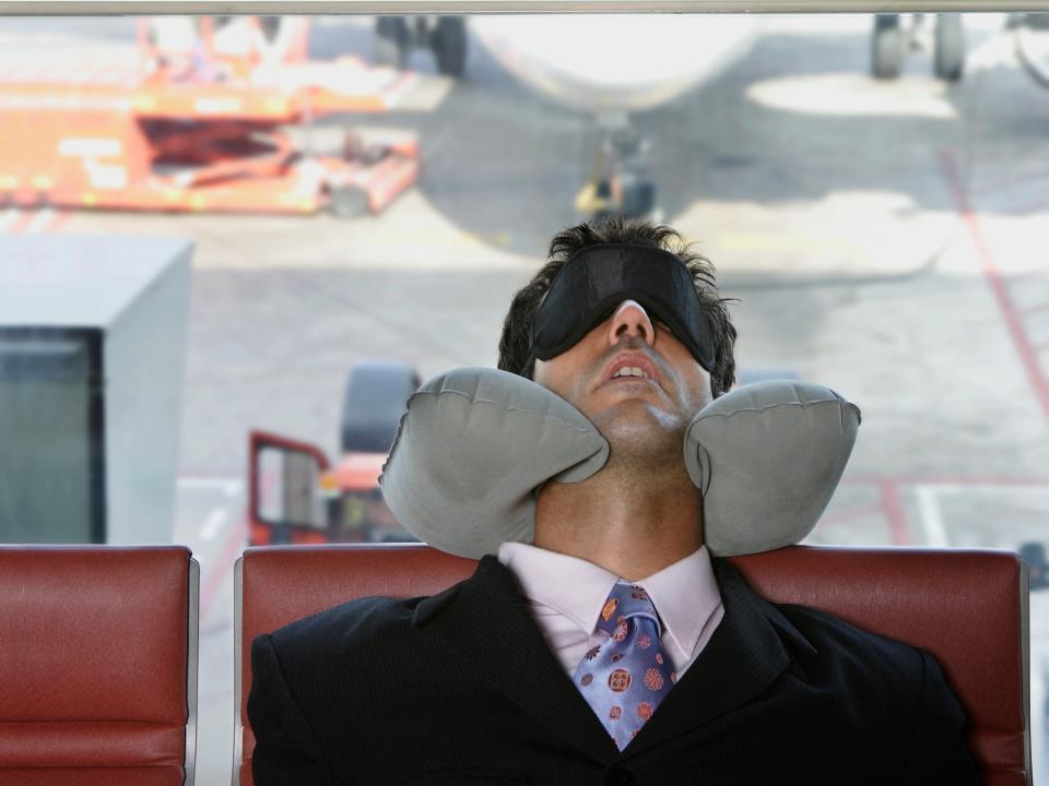 Man sleeping in an airport with a neck pillow and an eye mask