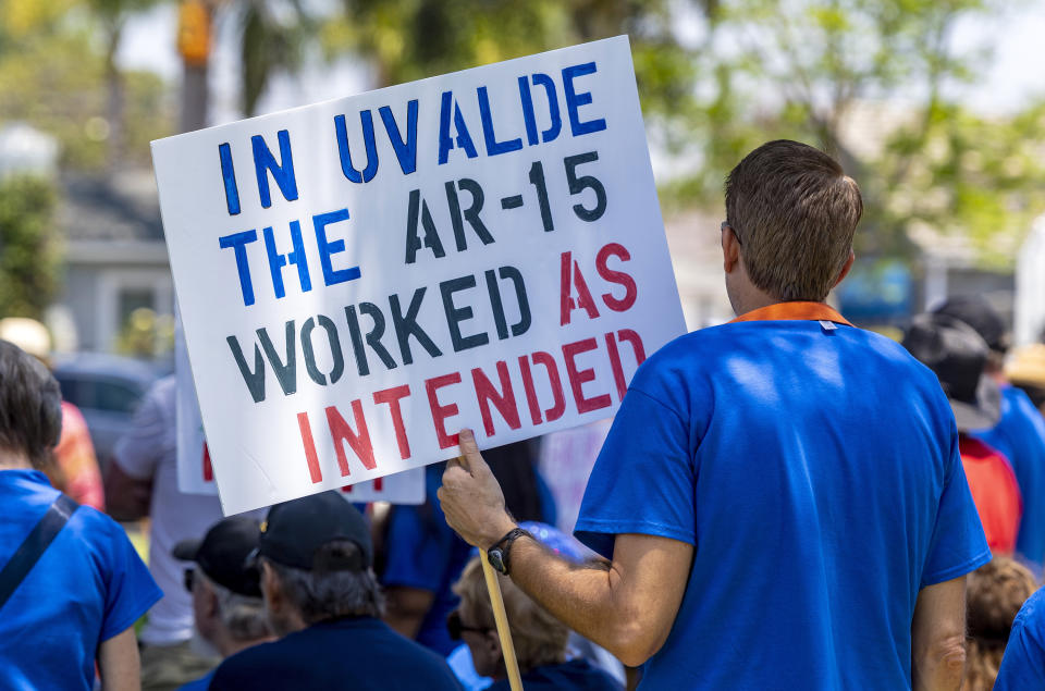 A person holds a sign that says "In Uvalde the AR-15 worked as intended"