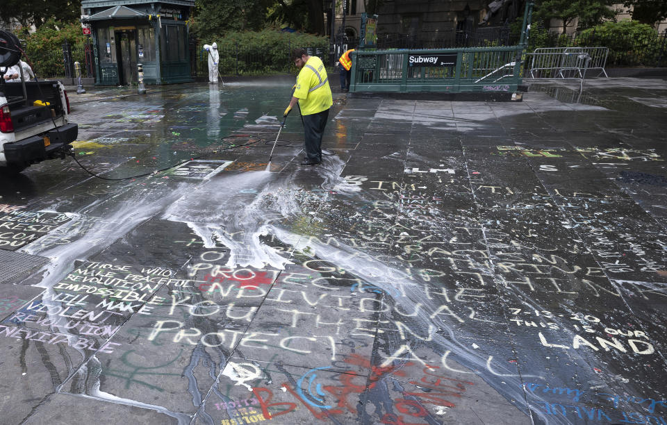 A city worker power washes graffiti from a park adjacent to City Hall, Wednesday, July 22, 2020, in New York. Police in riot gear cleared the month-long encampment of protesters and homeless people from the park earlier Monday morning. (AP Photo/Mark Lennihan)