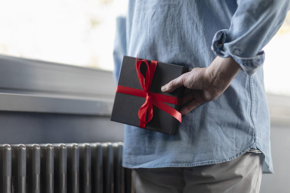 A man holding a box with a red bow on it behind his back.