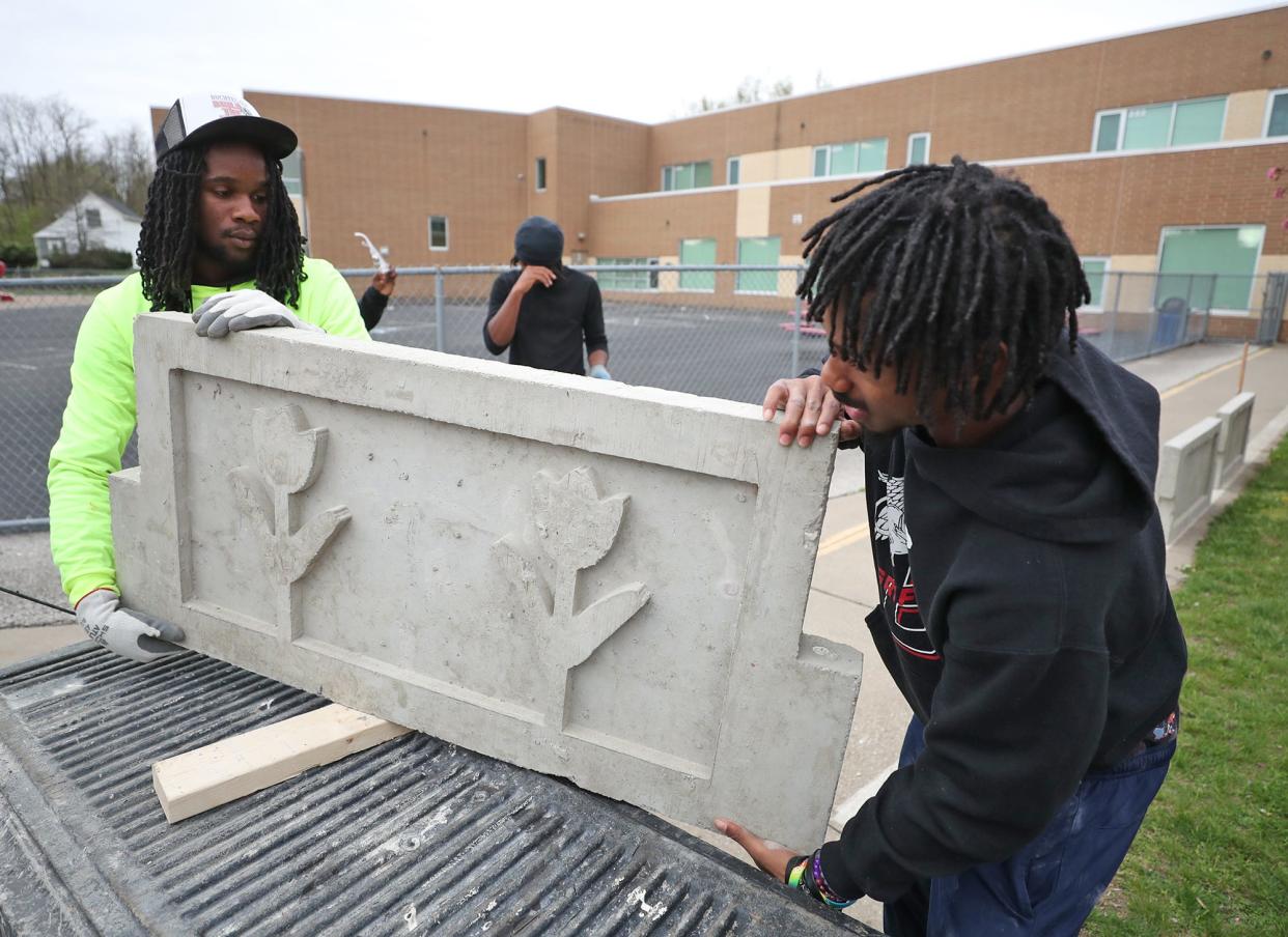 Former Helen Arnold CLC student James Bethune, 18, left, and his Buchtel CLC masonry classmate Zyaire Lewis, 18, lift a decorated section of a planter at Helen Arnold CLC on Wednesday. The Buchtel CLC masonry students were installing concrete planters they created to replace the wooden ones at Helen Arnold CLC.
