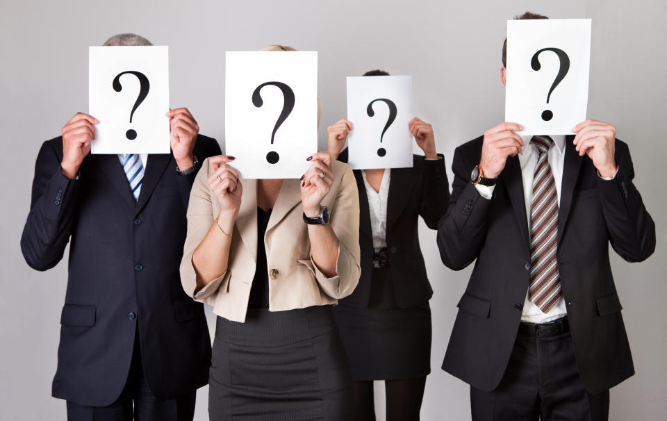 Four business people holding papers with question marks on them in front of their faces