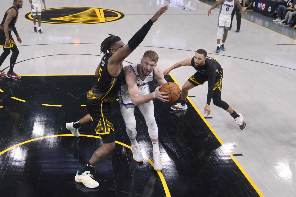 Sacramento Kings forward Domantas Sabonis, middle, drives to the basket against Golden State Warriors forward Kevon Looney, left, and guard Stephen Curry during the second half of Game 3 of an NBA basketball first-round playoff series in San Francisco, Thursday, April 20, 2023. (AP Photo/Jeff Chiu)