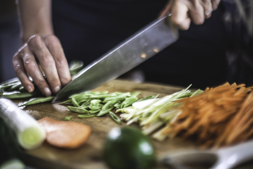 Close up shots of the cook's hands, finely slicing carrots, leeks and beans for a Korean dish.