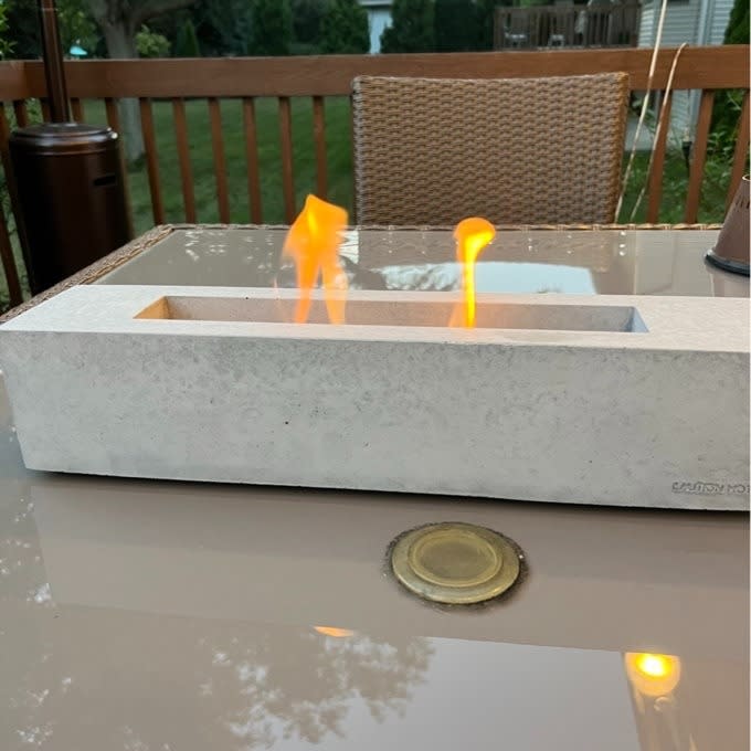 A tabletop fire pit with visible flames, set on an outdoor table for ambiance and warmth