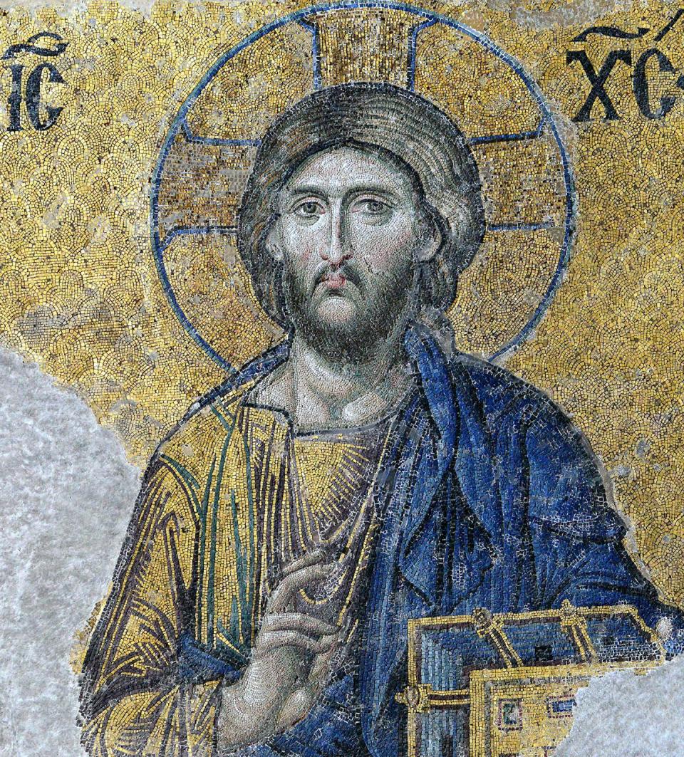 A painting of Christ on yellow mosaic; His hair is black and there is a halo around his head; He is dressed in a yellow and blue robe.
