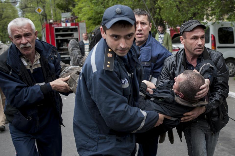 People carry a firefighter injured during an attack at a police station in Mariupol, eastern Ukraine, Friday, May 9, 2014. Fighting between government forces and insurgents in Mariupol has left several people dead. (AP Photo/Evgeniy Maloletka)