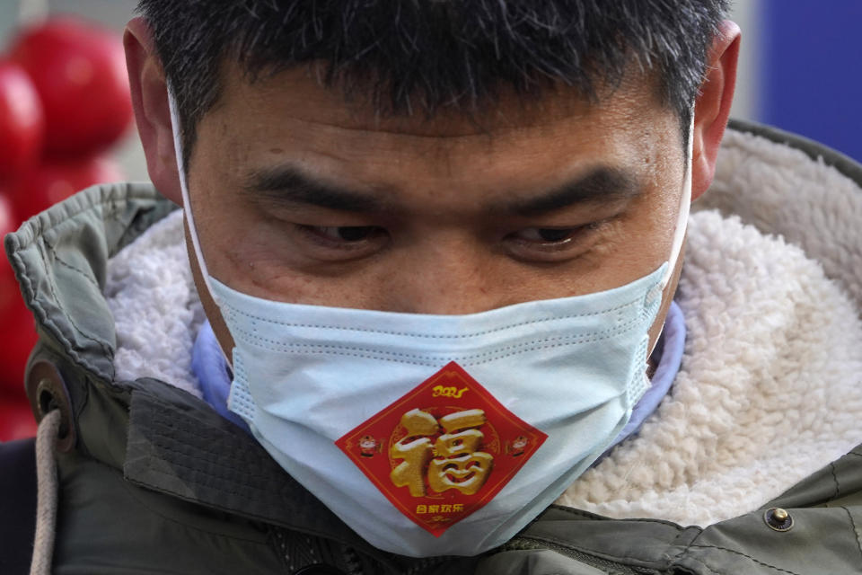 A street vendor wears a mask with a sticker which reads "Fortune" at a street stall near Wangfujing on the fourth day of the Lunar Chinese New Year in Beijing on Monday, Feb. 15, 2021. (AP Photo/Ng Han Guan)