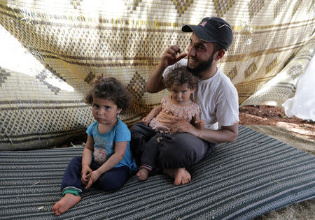 Ali, 25, a displaced Syrian farmer from the al-Ahmed family, holds his two daughters in an olive grove in the town of Atmeh, Idlib province, Syria, May 16, 2019. REUTERS/Khalil Ashawi