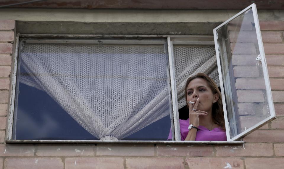 Myriam Roncancio se asoma por una ventana para fumar un cigarrillo el 28 de julio del 2020. Roncancio se separó de su marido en medio de la pandemia del coronavirus y vive con sus dos hijos en el departamento de sus padres en Bogotá. La cuarentena asociada con la pandemia está aumentando las tensiones domésticas y causando divorcios. "De un momento a otro, mi vida cambió", dice Roncancio, quien se separó luego de que ella y su marido se quedasen sin trabajo y la relación dejó de funcionar. (AP Photo/Fernando Vergara)