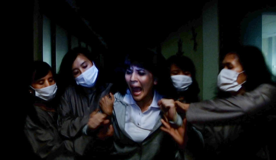 A group of women in masks holding onto a screaming woman